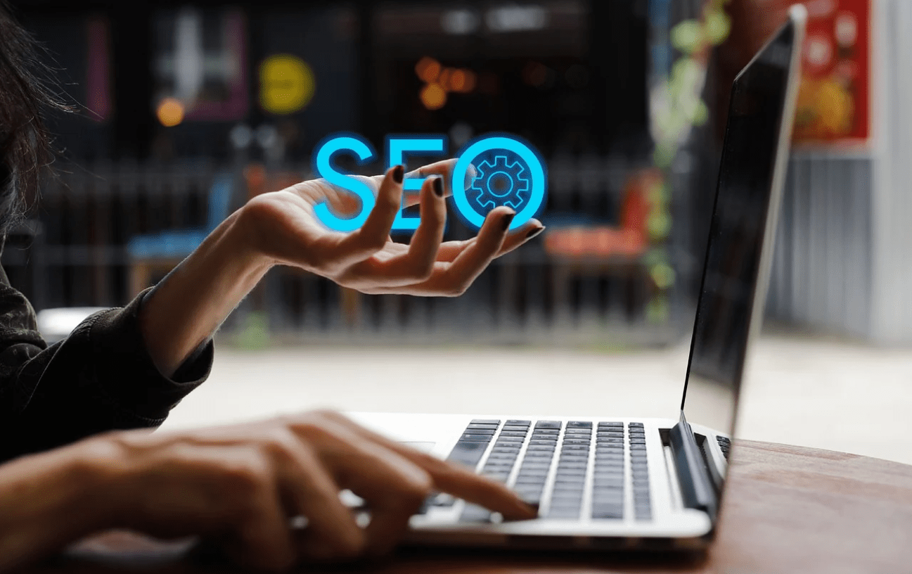The image shows a person multitasking, using a laptop with one hand while holding the letters "SEO" in the other hand.